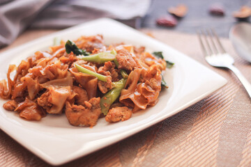 Stir fried Noodle with black soy sauce served in a white plate. on the black wooden table or what we call 