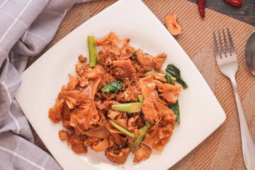 Thai Soy Sauce Fried Noodles served in a white plate. on the black wooden table or what we call 