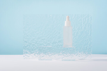 Serum cosmetic bottle with peptides and retinol on acrylic blocks on blue background. Hyaluronic...