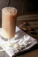 Iced coffee served on a black wooden table with Millingtonia hortensis flowers.