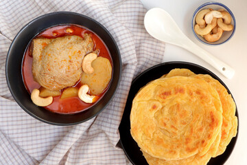 Chicken Massaman curry served with roti parata or roti canai on old wooden table. Delicious Thai food. 