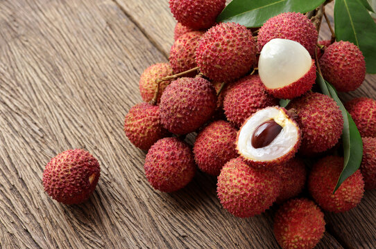 Fresh ripe lychee fruit and peeled lychee with green leaves on wooden background. rustic style, from above