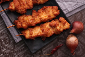 Fried pork skewers served on a black plate.