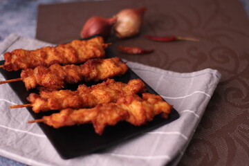 Fried pork skewers served on a black plate.