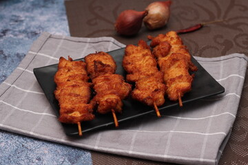 Fried pork skewers served on a black plate.