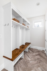 A modern farmhouse foyer or mud room with herringbone tiled floors, a white coat rack, and wooden...