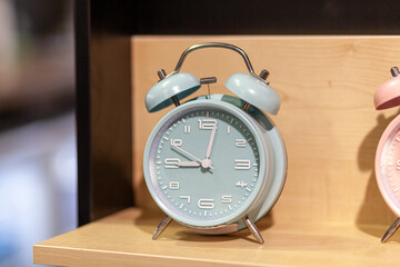 Naklejka premium Round alarm clock on the store shelf close-up. Sale of various watches and alarm clocks of different colors. Retro alarm clock on the table, vintage tone.