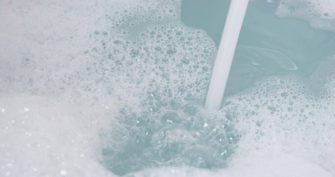 Bathroom with white bathtub full of warm water with thick layer of aromatic bubbles for relaxation. Preparation of taking bath at home or in hotel indoors. Spa, relaxation after a hard day