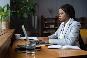 Serious frowning african entrepreneur ceo woman sit at workplace desk look at laptop screen read email from partner concerned. Focused businesswoman type response to customer with strategy explanation