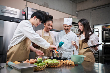Fototapeta na wymiar Hobby cuisine course, senior male chef in cook uniform teaches young cooking class students to prepare, mix and stir ingredients for pastry foods, fruit pies in restaurant stainless steel kitchen.