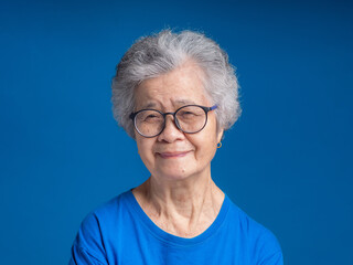 Senior woman with short gray hair looking at the camera with a smile while standing over a blue background