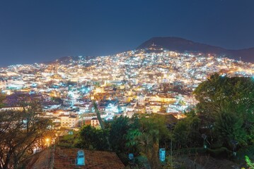 Lights of the night city on the slope of the mountain. The light of lanterns and windows of houses with colonial architecture. Dark blue night sky. Narrow streets of Taxco in Mexico