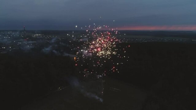 Aerial view of Fireworks at the Village stadium in the night. Stadium in the forest on the outskirts of the village. Lightning flashes on the sky, a thunderstorm begins. Around you can see houses, for