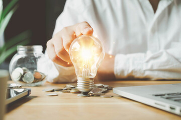 businessman holding lightbulb on coins stacking on desk with note for planning money finance.Saving money, saving money concept putting money coin stack growing business concept.