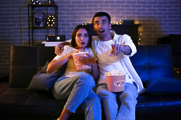 Naklejka premium Shocked young couple with popcorn watching movie at home in evening