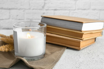 Holder with burning candle and books on table, closeup
