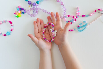 White rosary on a beige background. Small children's hands