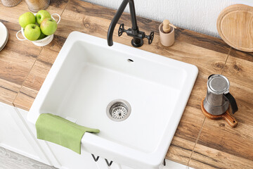 Wooden counter with kitchen utensils, fresh apples and ceramic sink near light wall