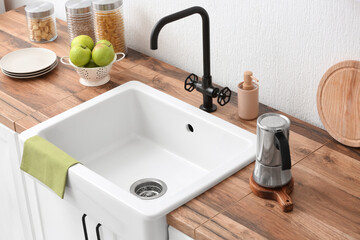 Counter with kitchen utensils, fresh apples and ceramic sink near light wall