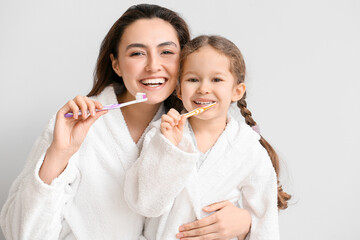 Little girl with her mother brushing teeth on light background - obrazy, fototapety, plakaty