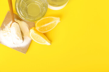 Baking soda, ripe lemon and glass of water on yellow background