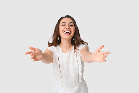 Happy young woman opening arms for hug on grey background