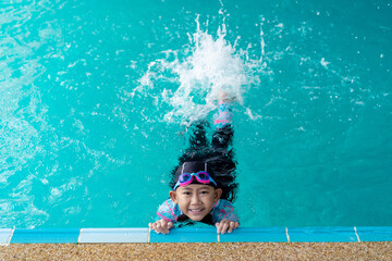 Asian child little girl wearing swimsuit and cap with goggles on edge swimming pool. Learn to swim...