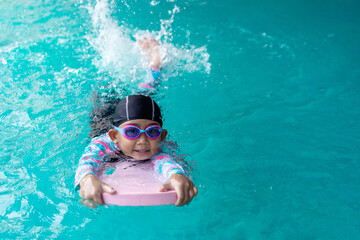 Asian child little girl swims with board in the pool. Swimming lesson idea concept
