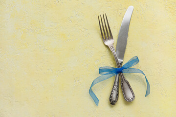 Knife and fork with ribbon on yellow background, top view