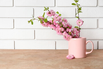 Cup with blooming branches on table near white brick wall