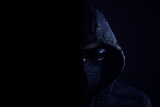 Stylish man in dark hoodie with black glasses and mask dark background, hacker, attacker and bandit.