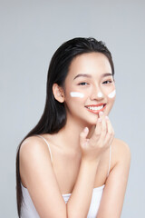 Beauty portrait image of pretty asian woman smiling and applying face cream isolated over light...