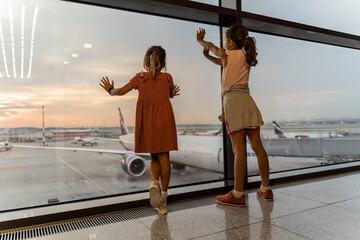 Little sister girls together at the airport waiting for boarding near the big window. Adorable...