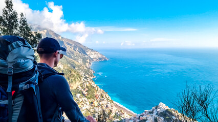 Hiking man with backpack enjoying panoramic view on the coastal town Positano and Praiano. Trekking...