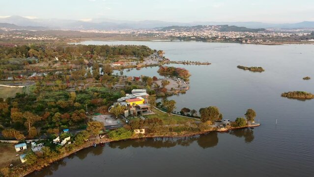 Aerial Circling Over Park And Shoreline Around Rawal Lake Shore With The City In The Background - Islamabad, Pakistan