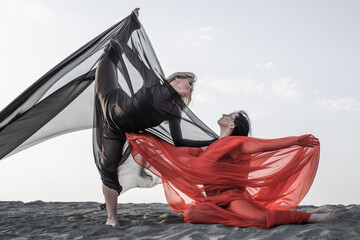 Two girls in black and red flowing fabric pose on sand dune