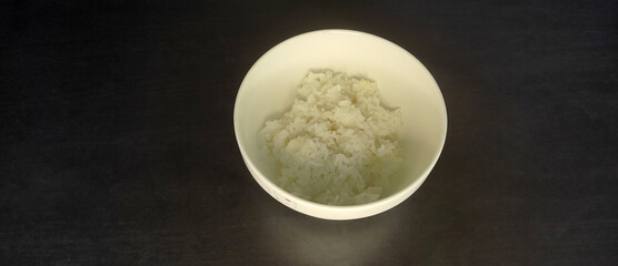 Cooked jasmine white rice, in a white bowl, on a black background. from top view
