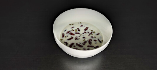 Homemade red bean and mung bean dessert topped with bean milk It's a healthy little dessert. in a white bowl black background made of wood