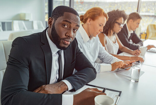 Portrait of African man in business suit sitting at table with co-workers