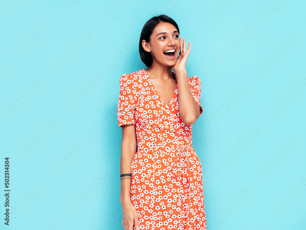 Wall mural young beautiful smiling female in trendy summer red dress. sexy carefree woman posing near blue wall