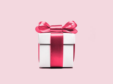 Pink gift box with shining red pink ribbon bow on pink background. Gift or holiday concept. Mothers Day, birthday wedding or St Valentines day banner with copy space. Minimal monochrome