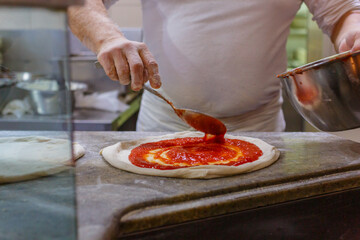 Pizzaiolo napoletano mentre stende del sugo di pomodoro sull'impasto di una pizza napoletana sul...
