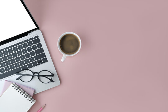 Above view laptop computer, eyeglasses, coffee cup and notepad on pink background with copy space.