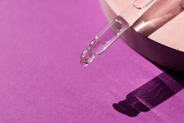 Pipette with serum or cosmetic liquid close-up on a purple background in soft focus. Beautiful shadow in the sunlight. Skincare products, natural cosmetic. Beauty concept for face and body care