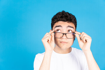 Hispanic teenager boy looking over glasses at copy space isolated on blue background.