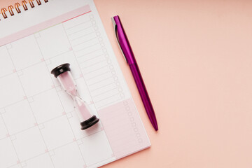 Hourglass with month planner and pen on a pink background. Time management and schedule concept