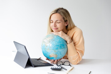 Fototapeta premium pretty young woman standing at height adjustable table plans her vacation with globe in hand and notebook and is daydreaming