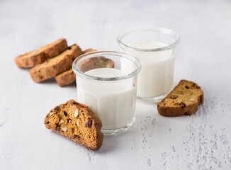 Two glasses of fresh milk and homemade pumpkin biscotti with cranberries and nuts on light gray background