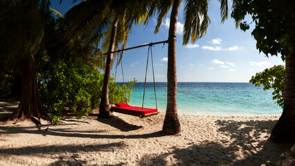 A Swing bed or wooden hammock between two coconut palm trees close to the beach in Maldive island
