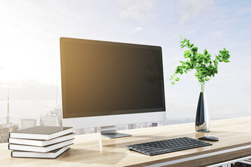 Close up of modern designer desktop with books, empty computer screen, decorative plant, supplies and bright city and sky view backdrop. Mock up, 3D Rendering.